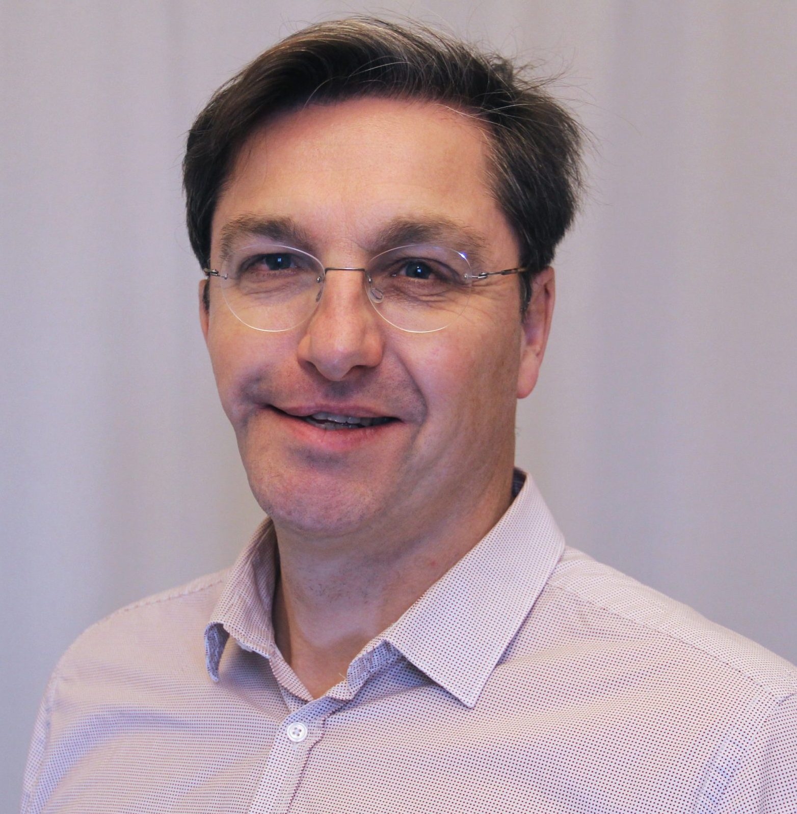 Man smiling with a white shirt and rimless glasses