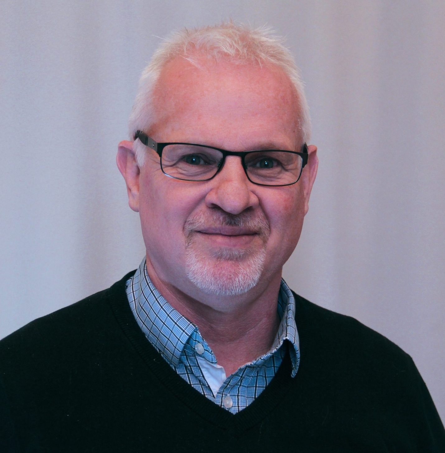 Smiling man with glasses, in a collared shirt with a black sweater over it.