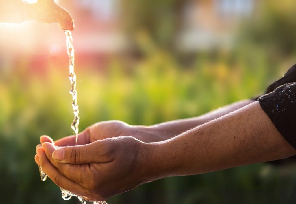 Hands receiving dripping water from a tap, with rays of sunshine in the backgorund