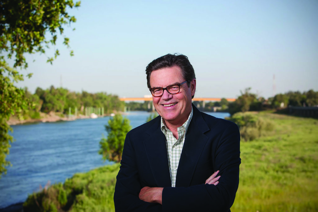 Stephen McCaffrey standing with hte arms crossed, a wide river with green shores in the background