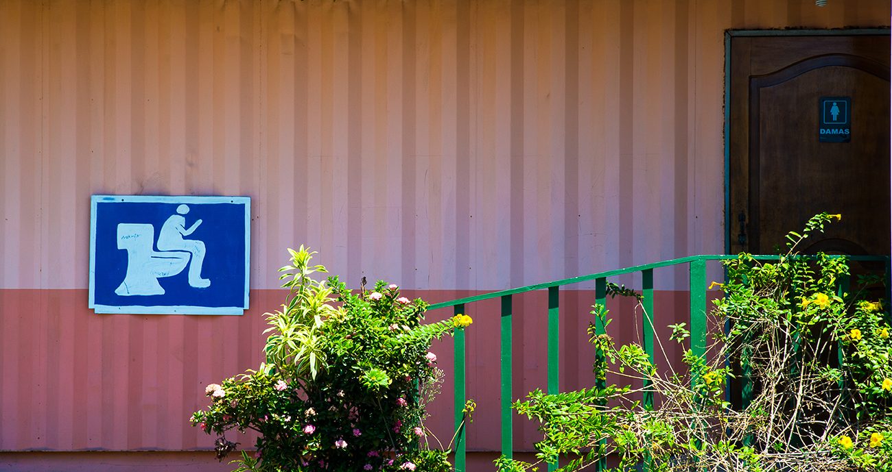 Blue toilet sign in Costa Rica showing a person sitting on a stool, at the entrance of toilets in a public space