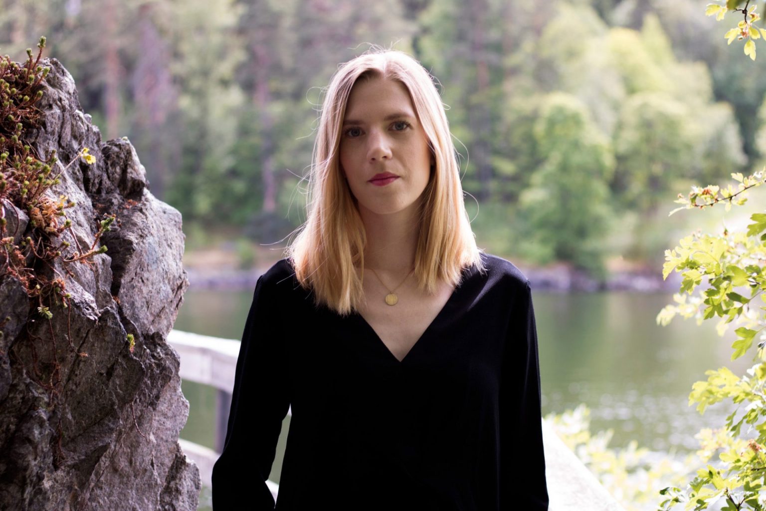 Emy standing in a nature scape with water, rocks and trees in the background