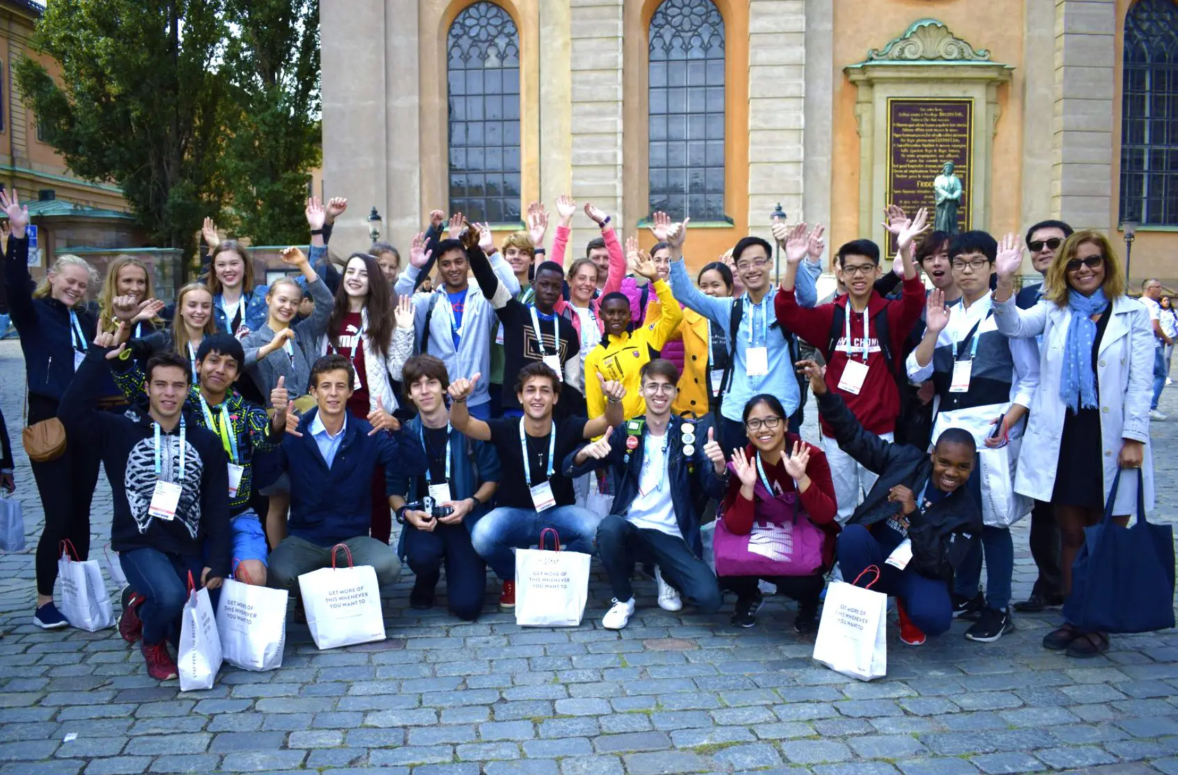 Students sitting down in a big group in front of a historic building facade