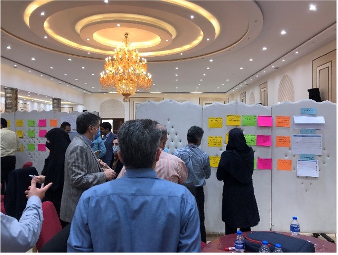 Workshop participants gathered in a hall and looking at a board with multicolour sticky notes