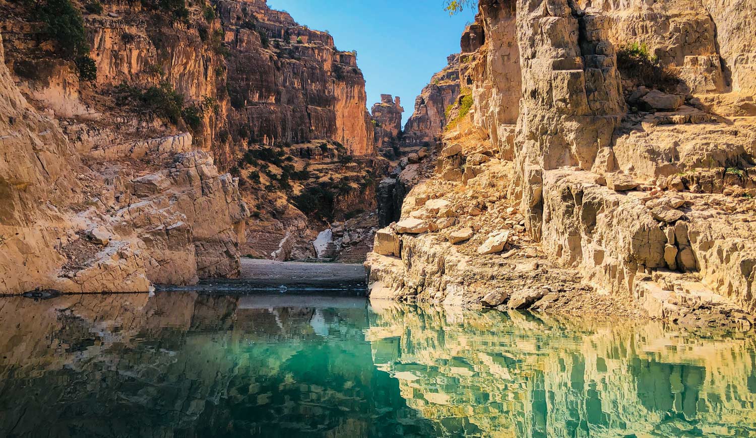 Aqua green lake with steep orange, sandstone cliffs behind, and a bright blue sky.