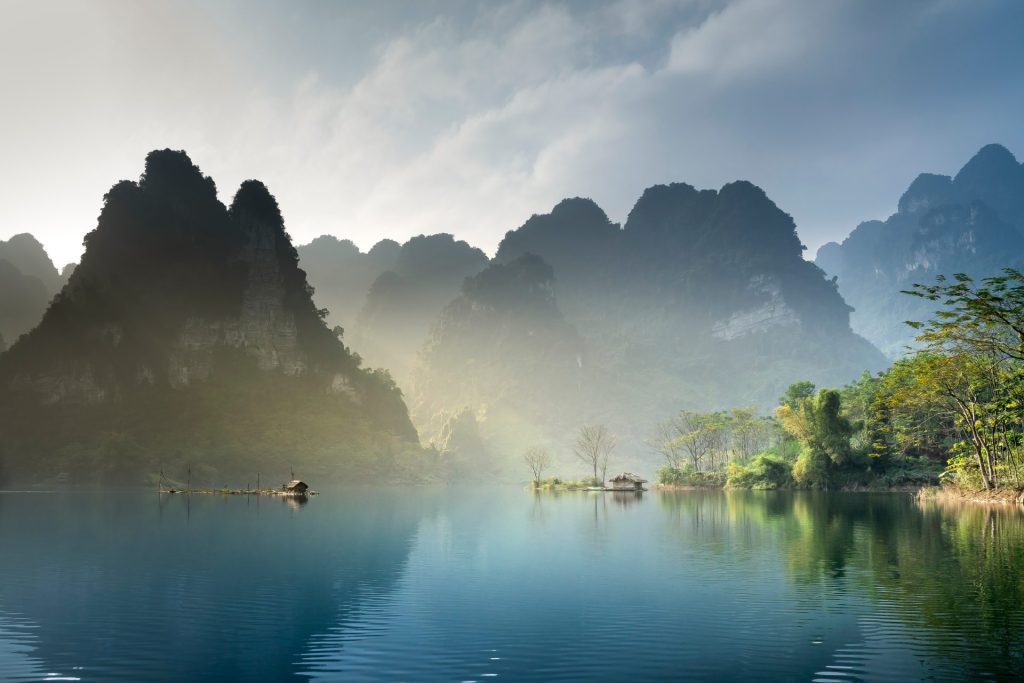 Image of a lake with mountains, trees in the backdrop and mist rising from the bottom.