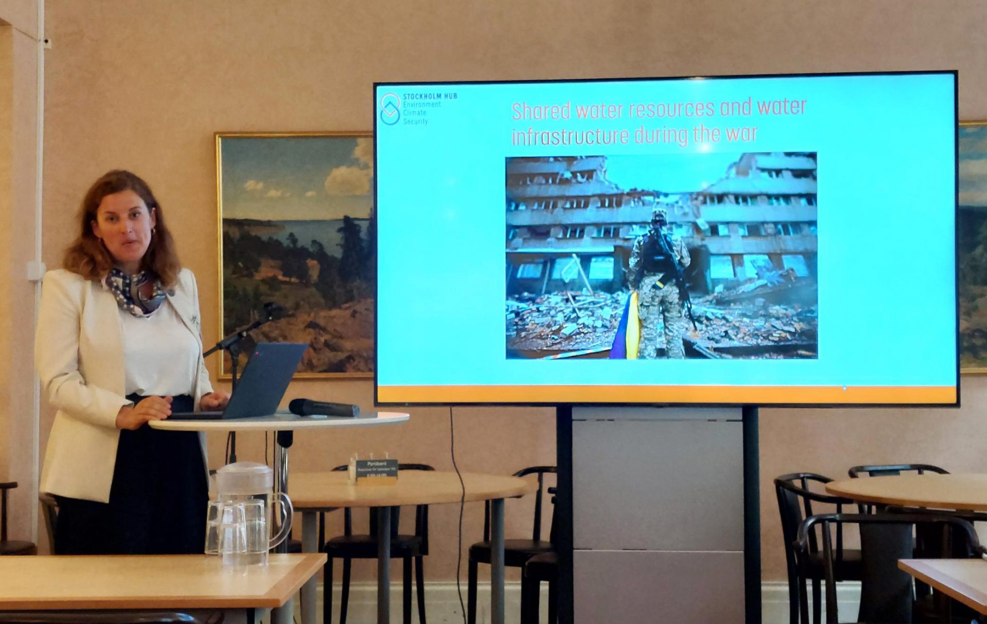 Dr Marina Klimes presenting in front of a screen where we can read "Shared water resources and water infrastructure during war"