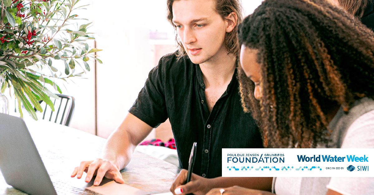 A white man and a black woman sitting side by side at a table, with a laptop and notebook