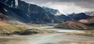 river flowing between high mountains with grey rainy sky